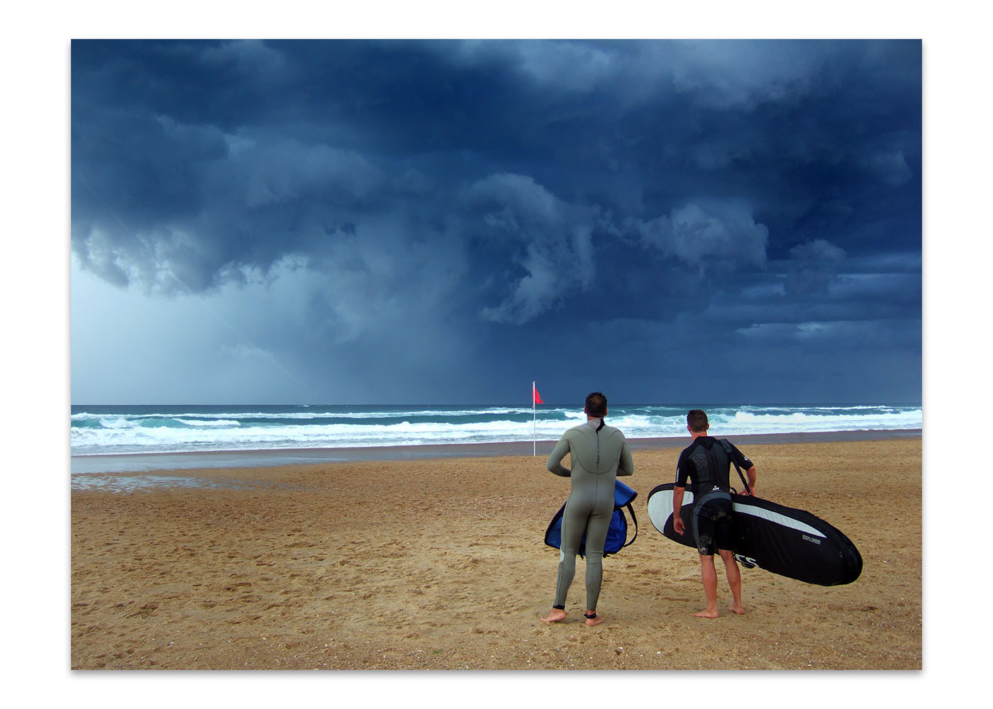 Deux surfeurs face à la mer, au loin de gros nuages orageux, ils hésitent à y aller