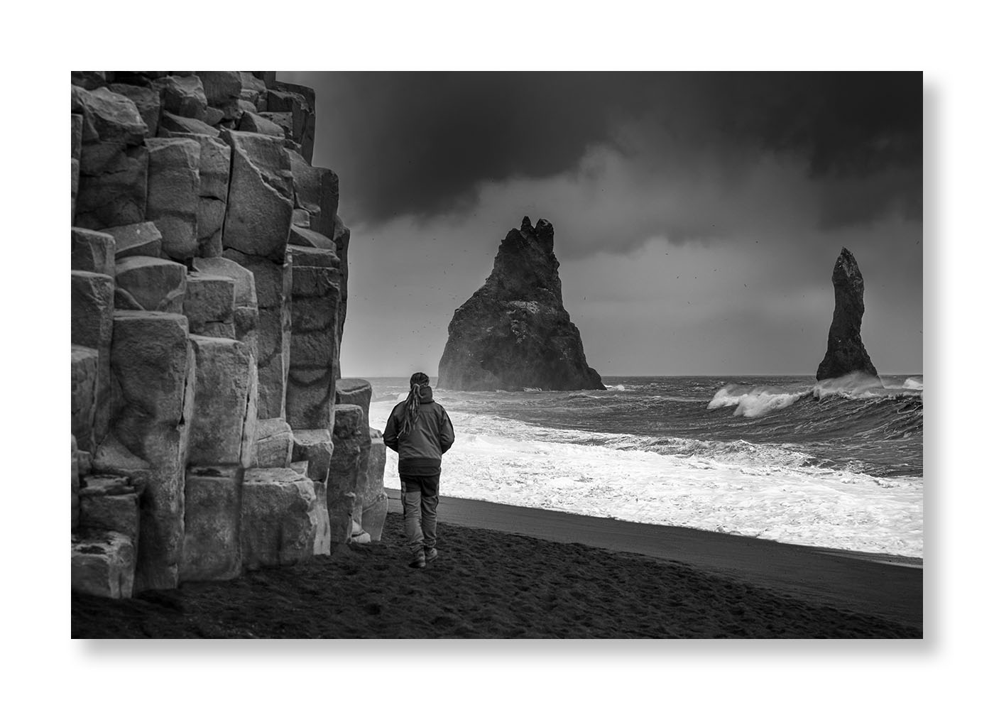 Un homme sur une plage près de rochers en colonne  face à la mer ou deux  aiguilles rocheuses sorte de l'océan