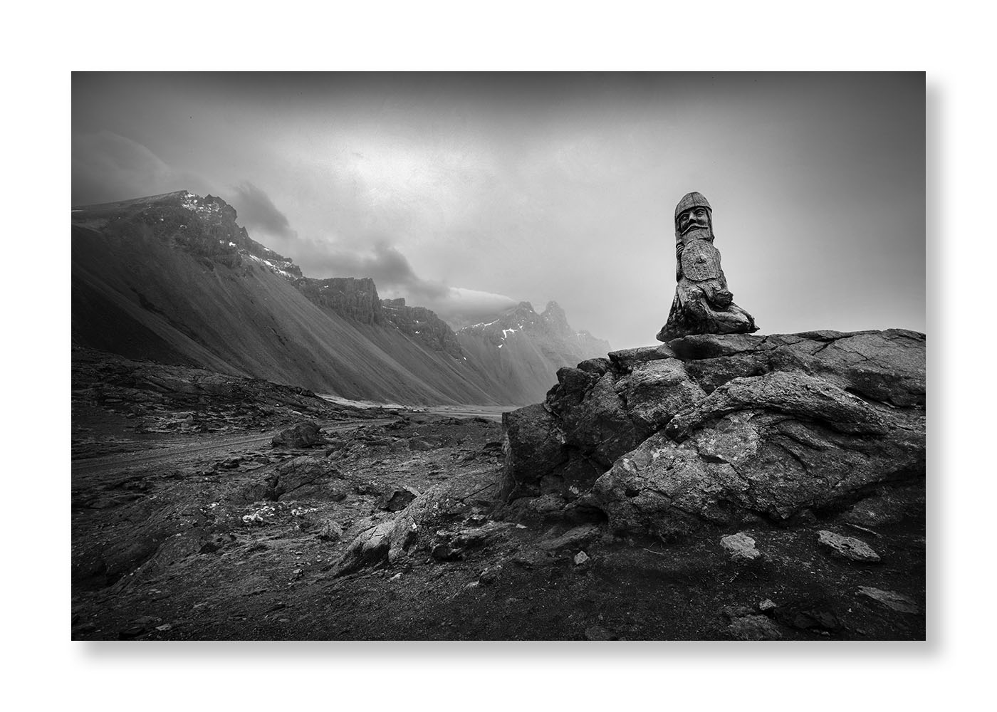 En premier plan une statue en bois vikings  en Islande sur rocher noir ciel lourd