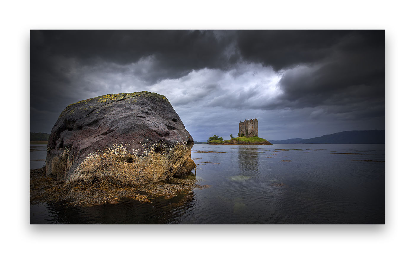 Un beau rocher en premier plan sur un lac écossais, au loin la silhouette d'un château fort.